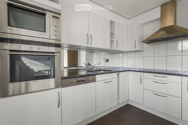 Modern kitchen with white cabinets, stainless steel appliances, and a dark countertop.