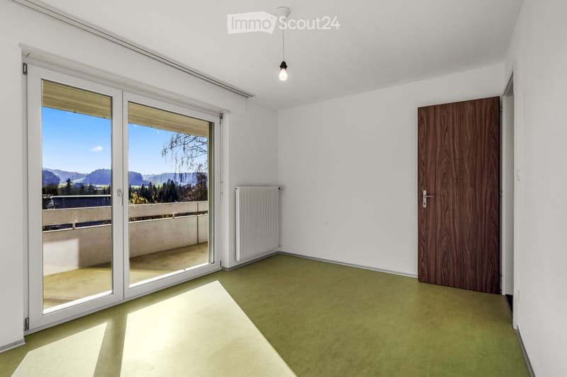 Empty room with white walls, green carpet, large sliding glass doors leading to a balcony with scenic mountain view.