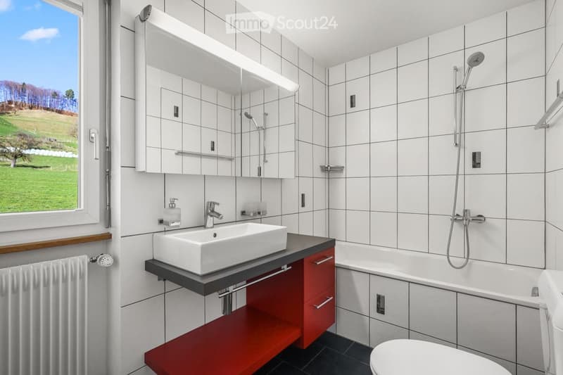 Modern bathroom with white tiles, a large window offering a scenic view, a sink with a modern faucet, a bathtub, a toilet, a mirror cabinet, and a showerhead.