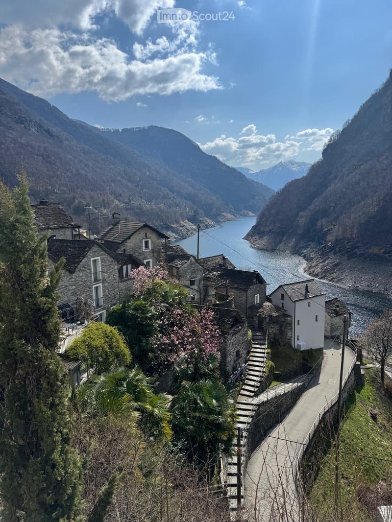 A picturesque village nestled in a mountainous valley, featuring stone houses, a winding road, and a serene lake in the background.