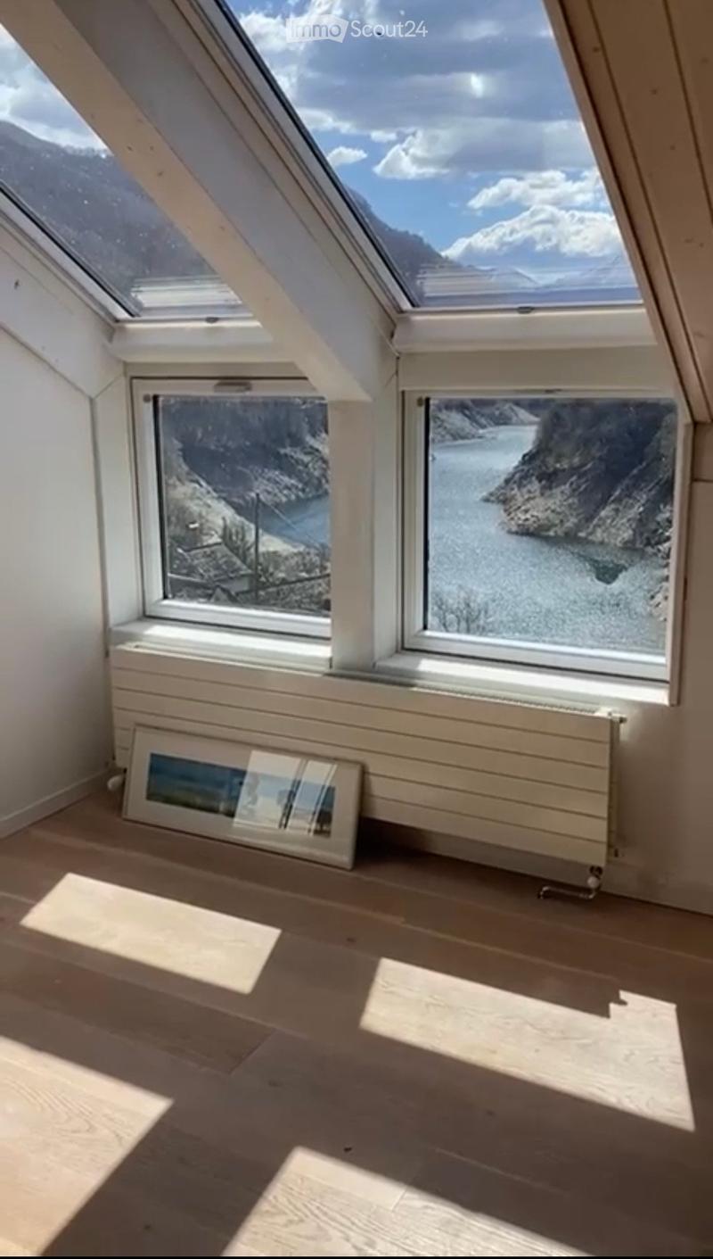 Empty attic room with wooden flooring, large skylights, and windows offering scenic views of a mountainous landscape.