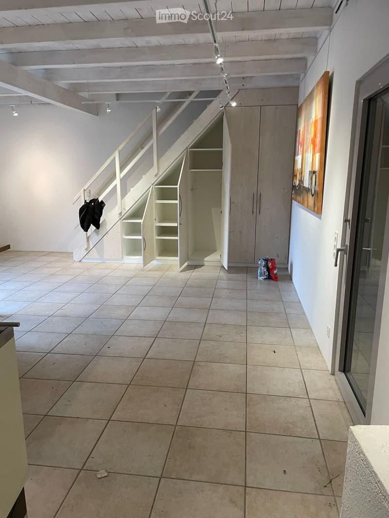 Empty hallway with tiled floor, white walls, built-in closet, staircase, and a few scattered items like a jacket and a water bottle.
