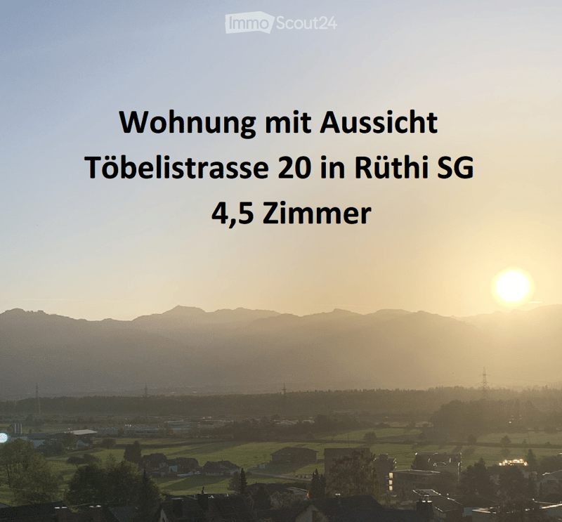 Panoramic view of a town with houses, fields, and distant mountains at sunset.