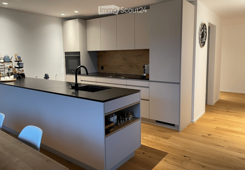 Modern kitchen with white cabinets, dark countertop, island, sink, and small dining area with a table and chairs.