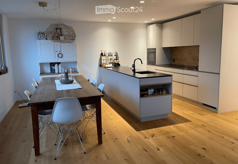 Modern kitchen with white cabinets, wooden floor, island, dining table, and chairs.