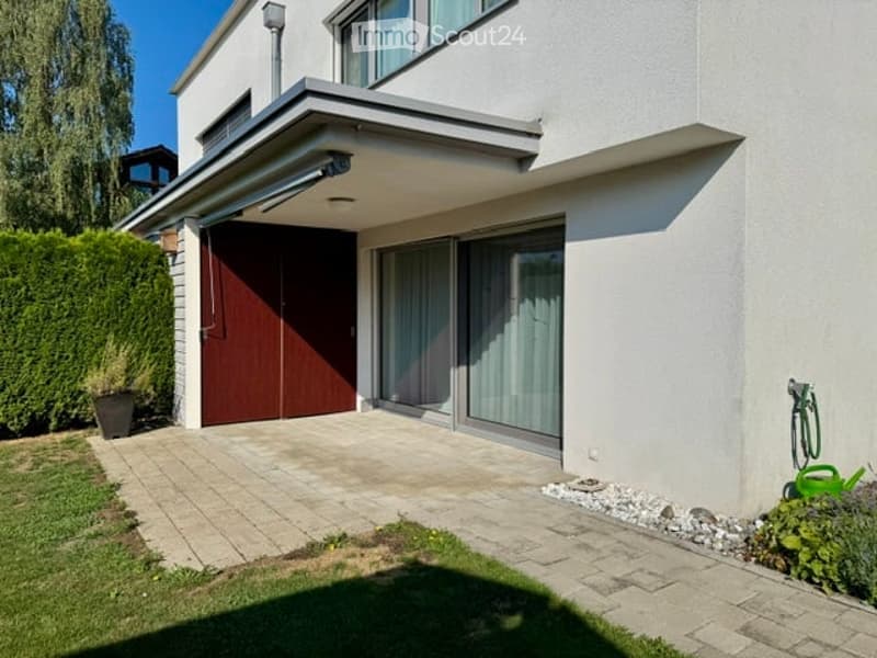 Modern two-story house with a garage, large windows, and a well-maintained garden area.