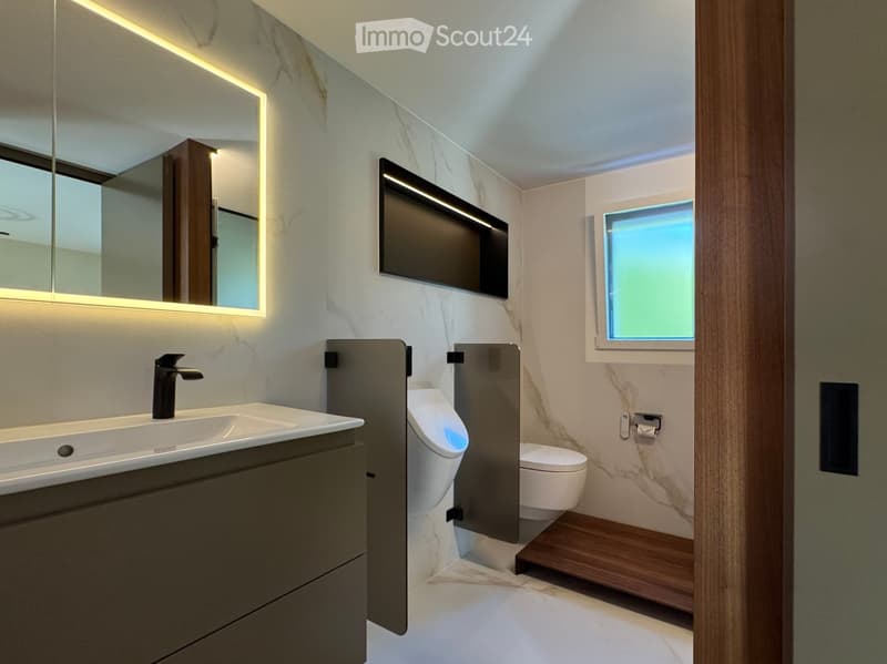 Modern bathroom with marble walls, a sink with a sleek faucet, a toilet, an urinal, and a mirrored cabinet with built-in lighting.