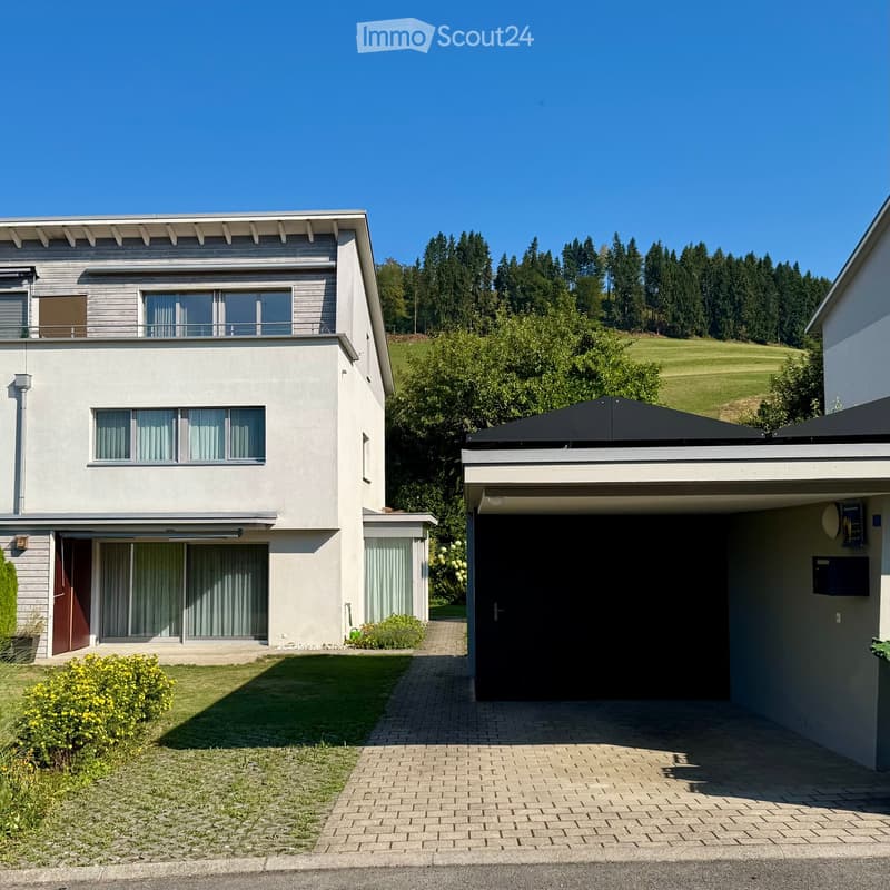 Two-story modern house with a garage, large windows, and a well-maintained garden.