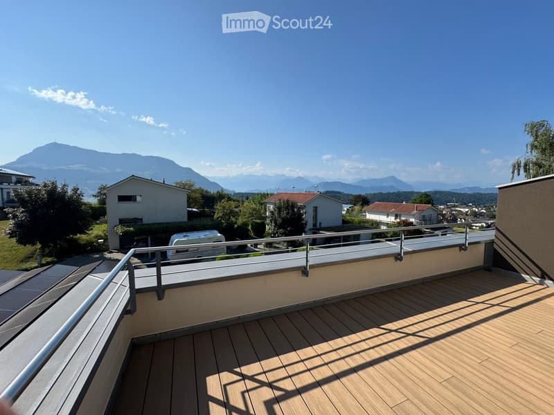 Wooden deck with metal railing, overlooking a suburban area with houses and distant mountains.