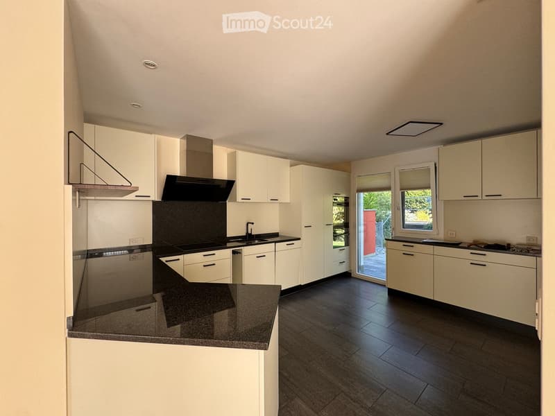 Modern kitchen with white cabinets, dark countertops, and a central island. Features include a range hood, sink, and ample storage space.