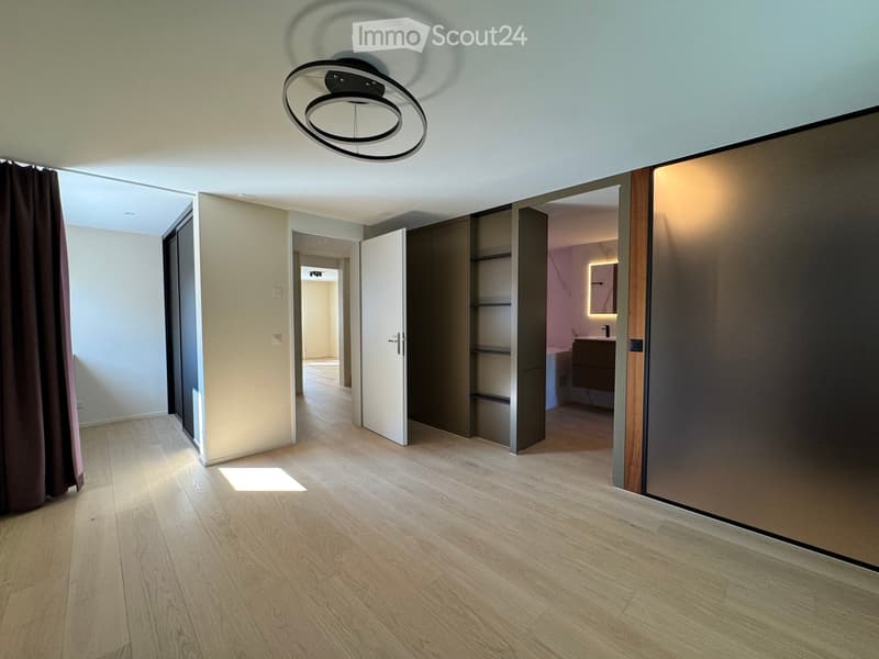 Empty hallway with wooden flooring, modern ceiling light fixture, and open doors leading to other rooms.
