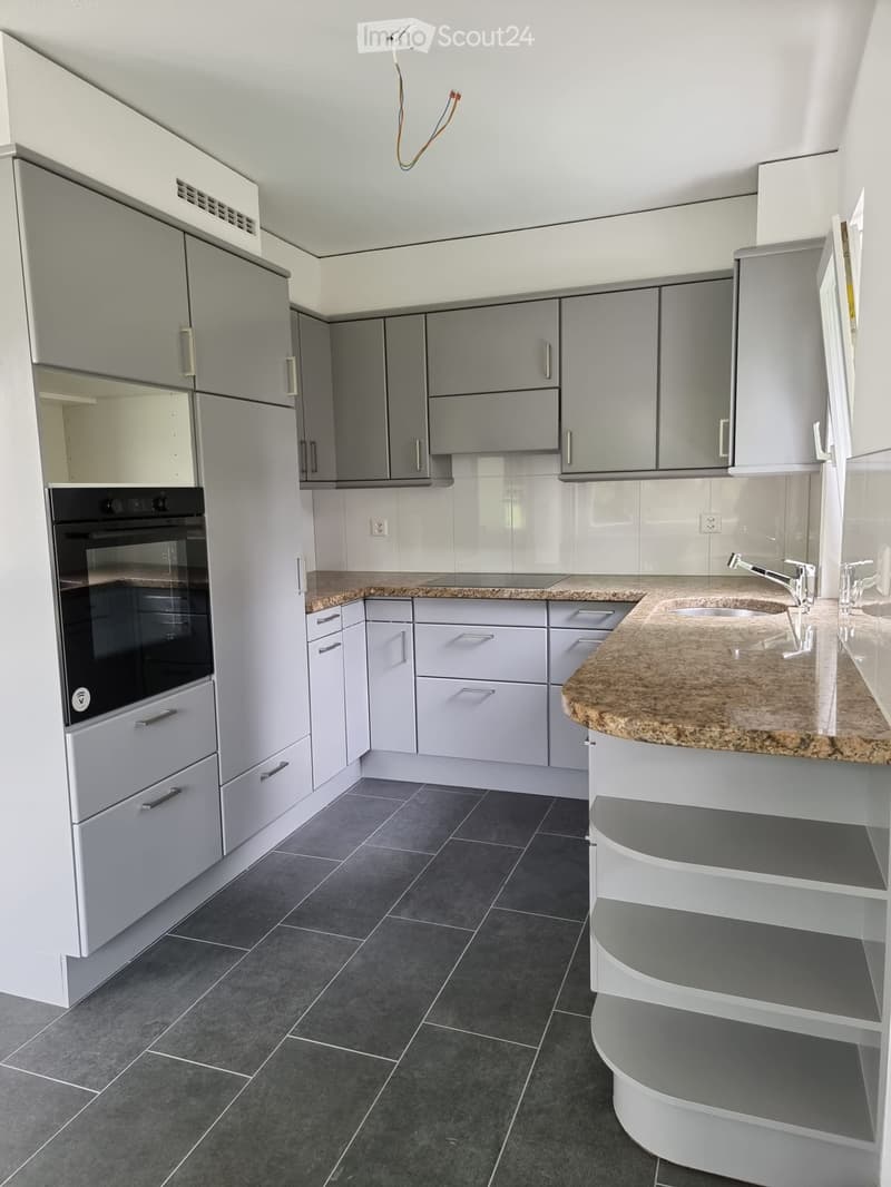 Modern kitchen with grey cabinets, granite countertop, dark tiled floor, and built-in oven.