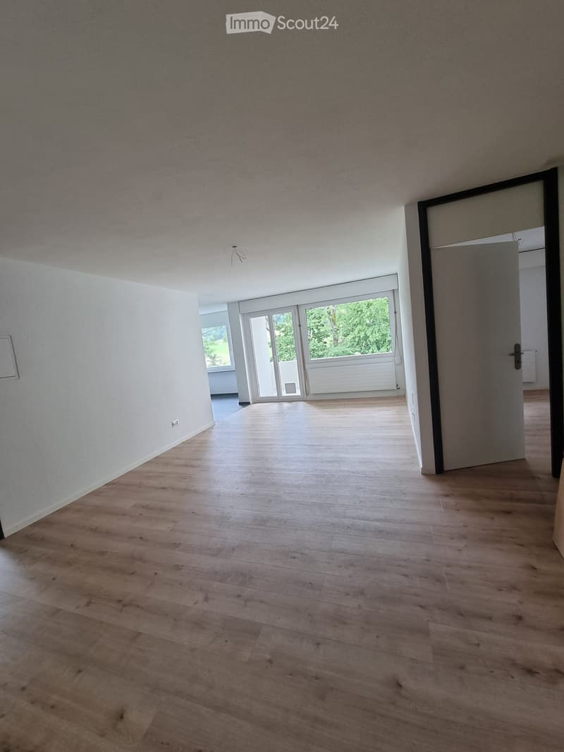 Empty room with wooden flooring, white walls, and large windows leading to a balcony area.
