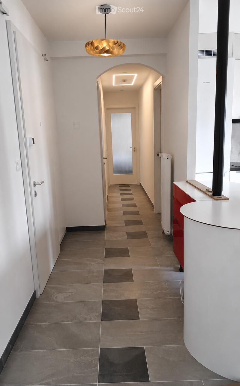 Modern hallway with tiled floor, white walls, arched doorway leading to another area, pendant light fixture, and a small cabinet with a sink visible on the right side.
