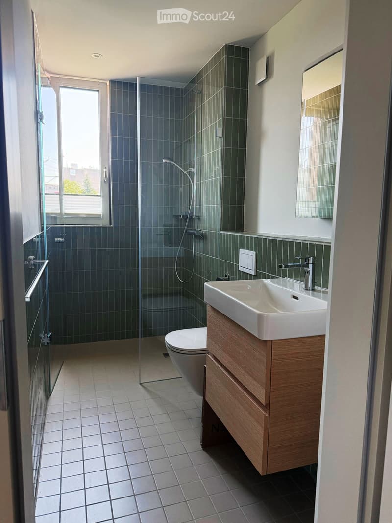 Modern bathroom with a white sink, wooden cabinet, toilet, glass-enclosed shower, and a large window providing natural light.