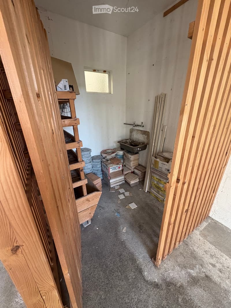Empty room with unfinished walls, carpeted floor, and scattered construction materials including a sink, boxes, and wooden planks.