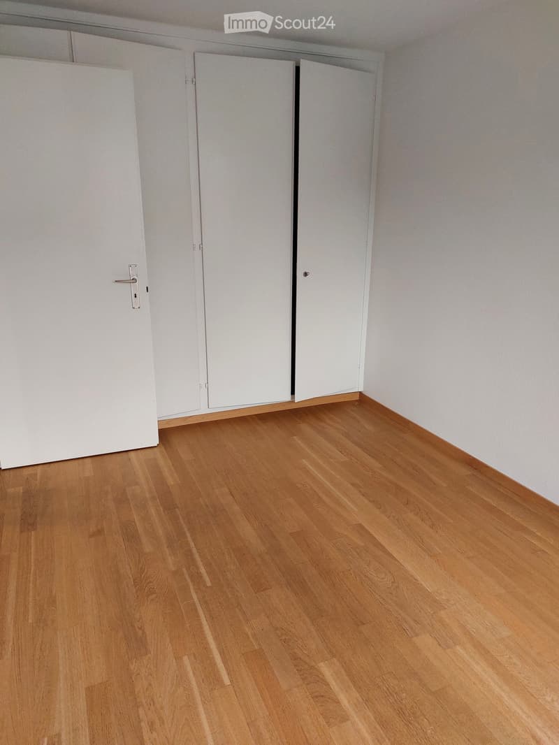 Empty room with light wooden flooring and white walls, featuring a set of white closet doors.