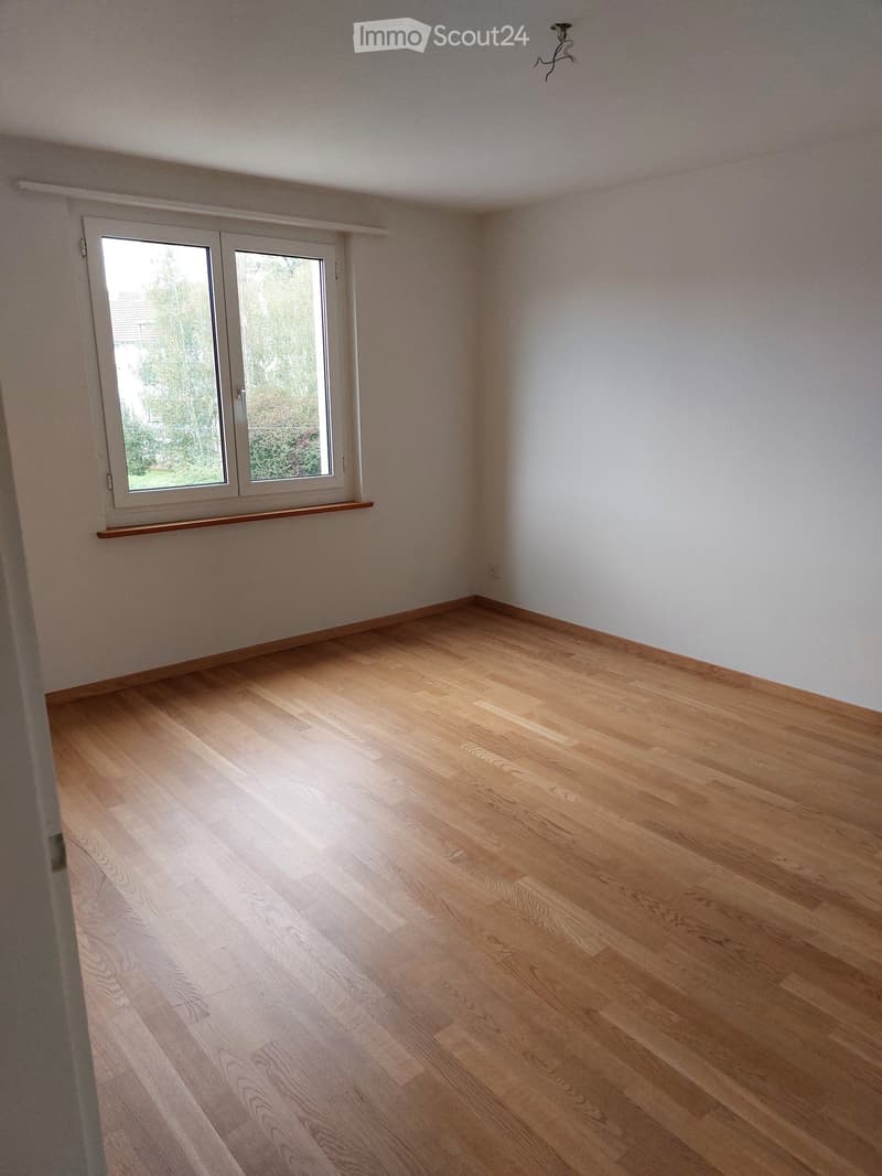 Empty room with light wooden flooring, white walls, and a large window with a wooden sill. No furniture or equipment is present.