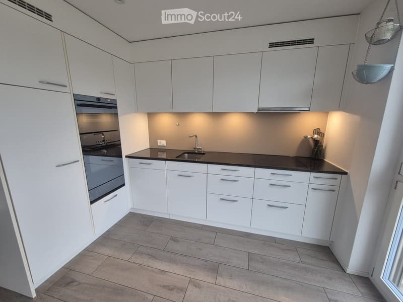 Modern kitchen with white cabinets, black countertop, and stainless steel appliances including an oven and sink.