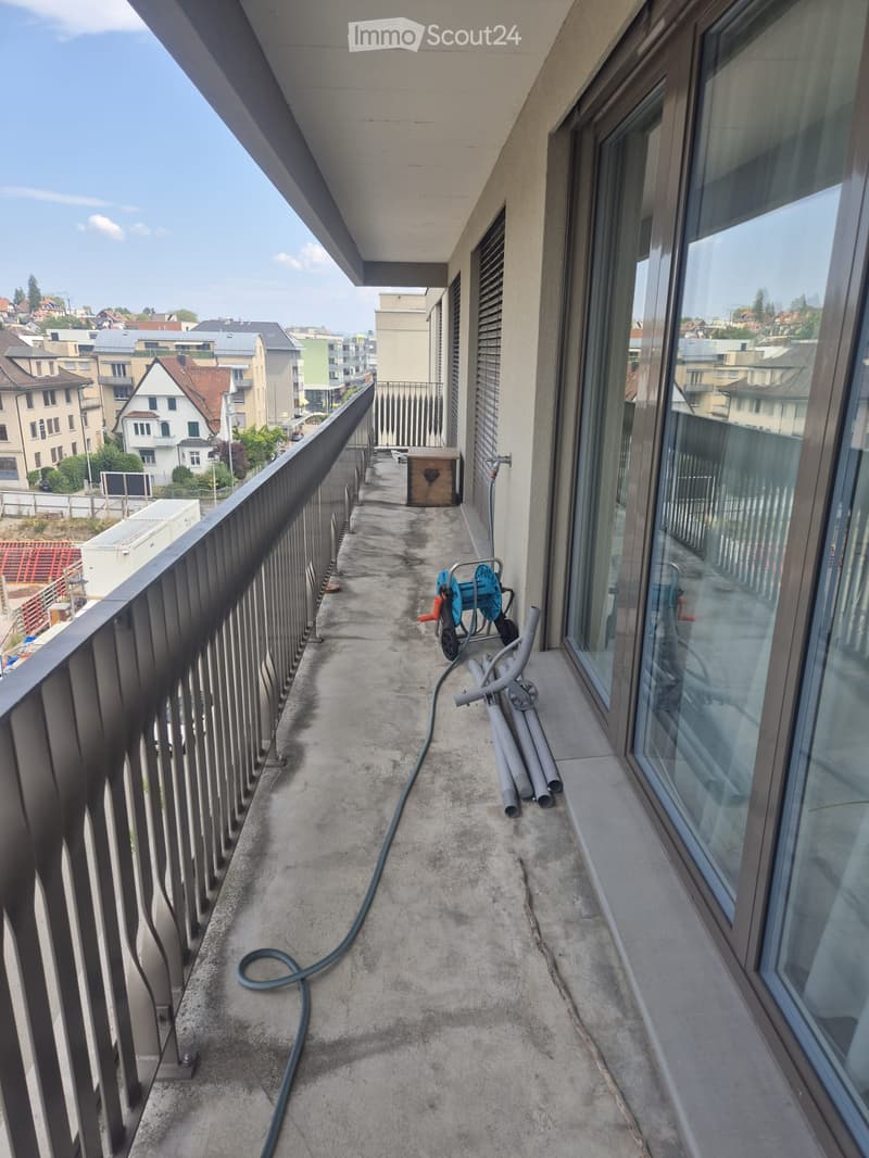 Balcony with metal railing, concrete floor, large windows, and a view of the city.