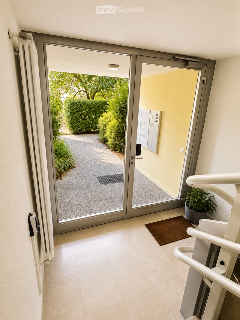 Hallway with tiled floor, white walls, sliding glass doors leading to a garden area, a small potted plant, and a brown doormat.