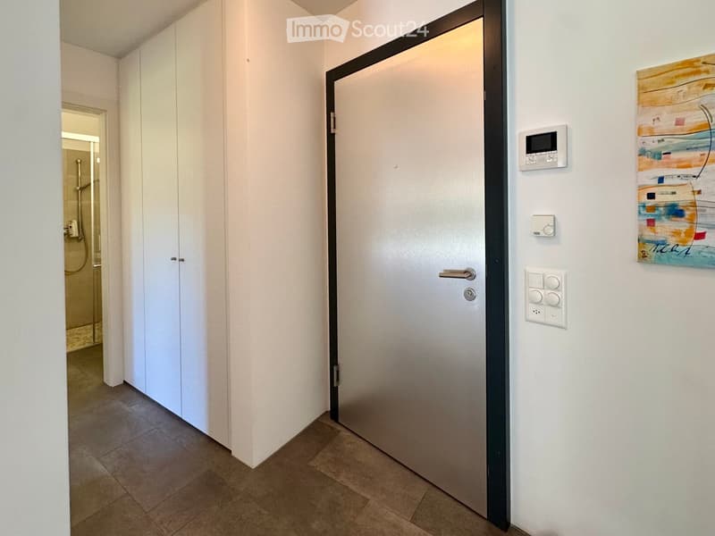 Modern hallway with tiled floor, white walls, closed door, and control panel on wall.