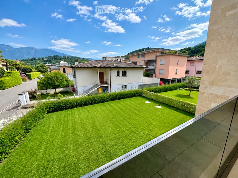 Well-maintained lawn with trimmed hedges, surrounded by residential houses and trees, with a scenic mountain backdrop.