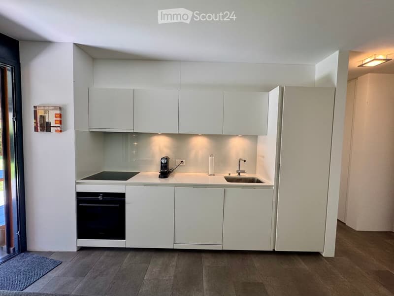 Modern, compact kitchen with white cabinets, a built-in oven, a sink with a faucet, and a coffee maker on the countertop.