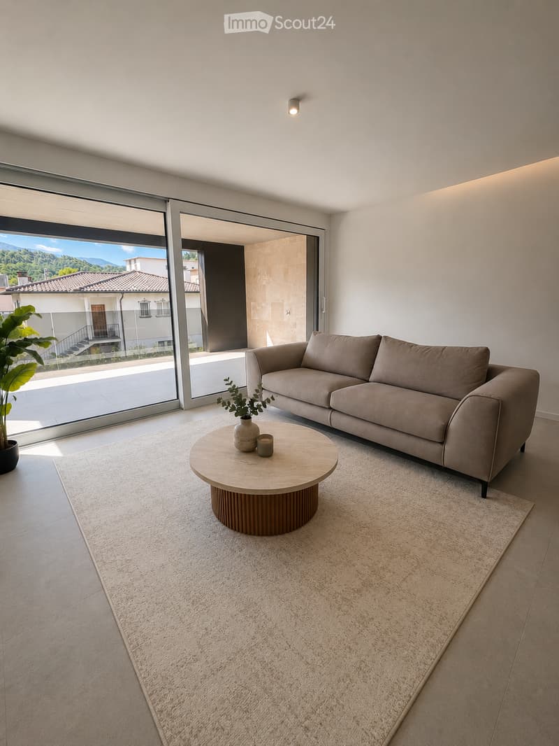 Modern living room with a beige sofa, round wooden coffee table, small vase with plant, and a large window offering a scenic view.