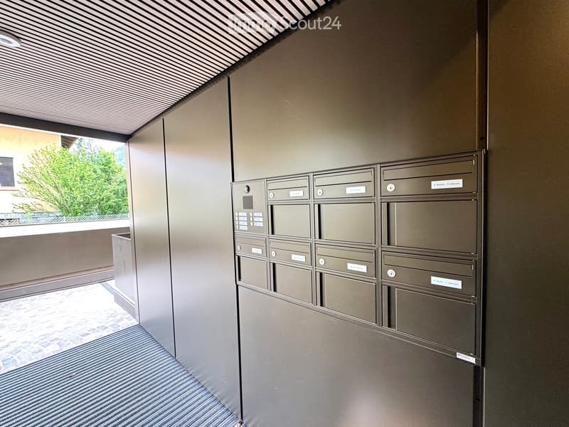 Corridor / Hallway. Modern hallway with mailboxes, striped carpet, and a view of greenery through a window.