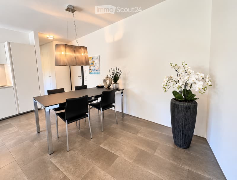 Modern dining area with a dark wooden dining table, four black chairs, a large pendant light, and decorative vases with flowers.