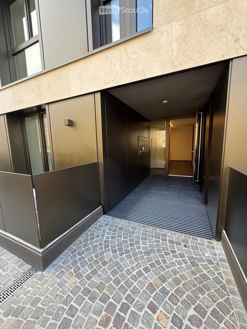 Corridor / Hallway. Modern hallway with cobblestone flooring, glass doors, and elevator access. The walls are light-colored with sleek metallic accents.