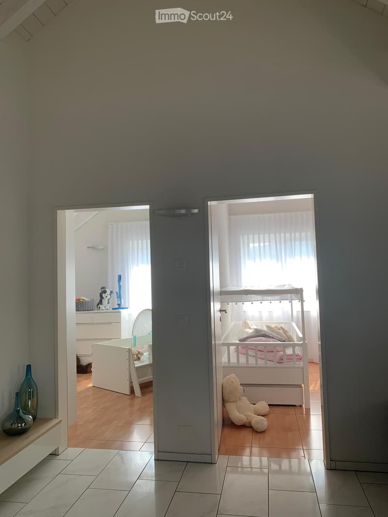 Interior room with white walls, white tiles, wooden floor, white drawers, toddler bed, stuffed toys, vases, and open windows with curtains
