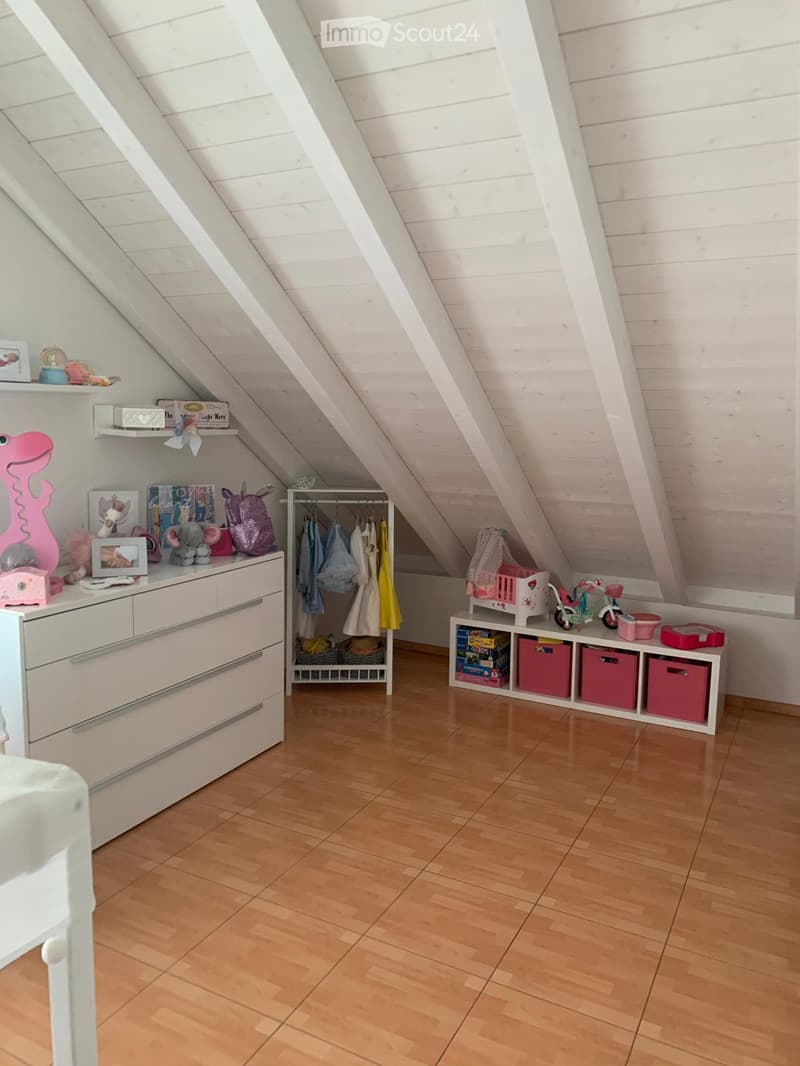 A room with white dresser, wooden floor, white ceiling, shelves with toys, clothes hanging on a rack