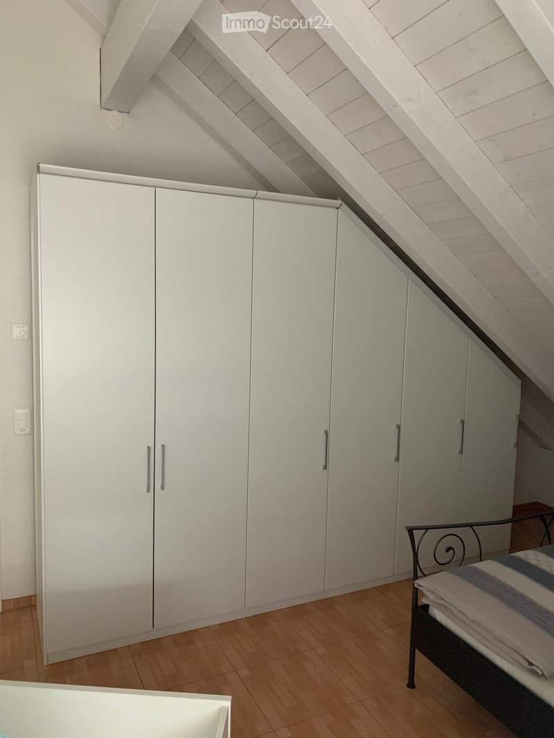 Room with large corner wardrobe, wooden floor, slanted ceiling, bed.