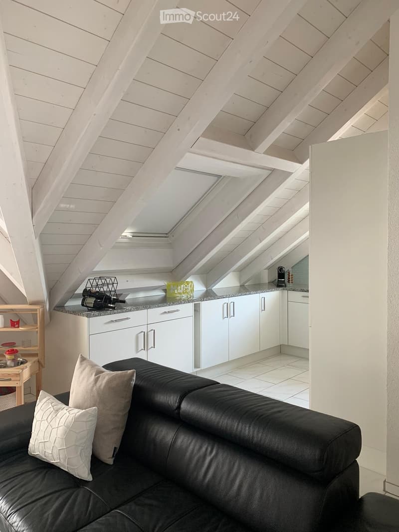 attic space with slanted ceilings, modern white kitchen with marble countertop, black leather sofa with pillows, small wooden table, white tile flooring