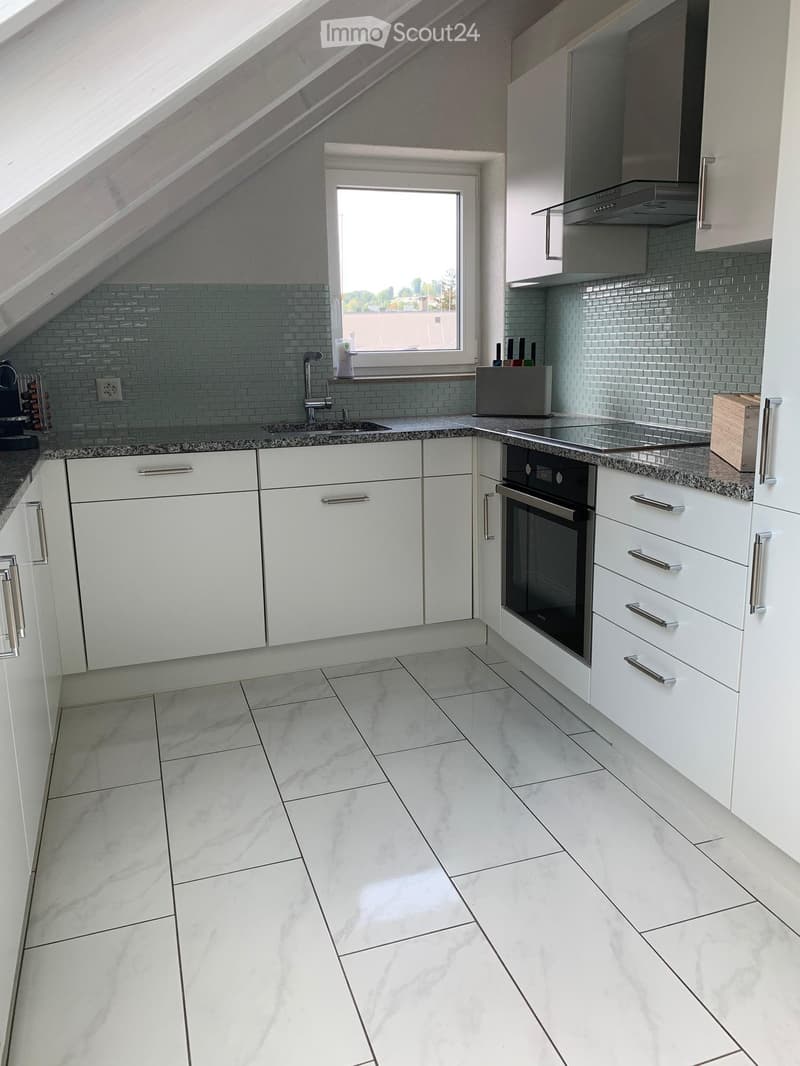 A contemporary attic kitchen with white cabinets, tiled backsplash, granite countertops, integrated oven, gas stove, and modern sink with a faucet. There is also a power outlet visible.