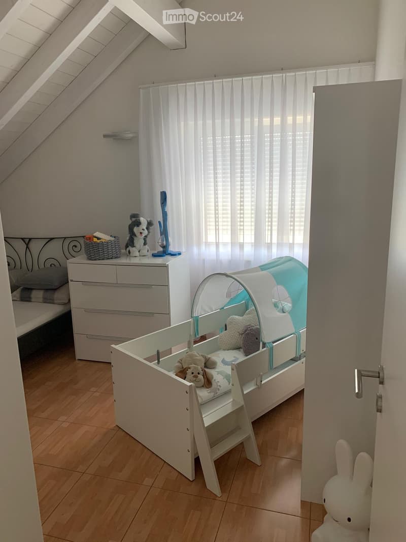 white toddler bed, toy dog, baby crib, white chest of drawers, white wall, wooden floor, window with white curtains