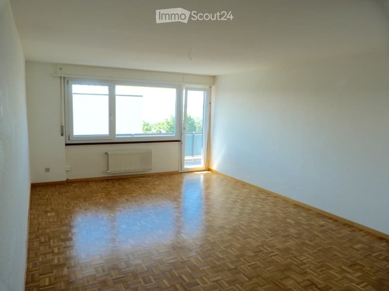 Empty room with wooden parquet flooring, light blue walls, large window, and sliding glass door leading to a balcony.