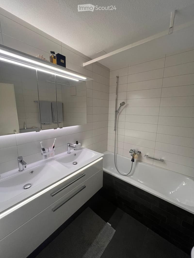 Modern bathroom with white tiles, double sink, large mirror, bathtub, walk-in shower, white cabinet