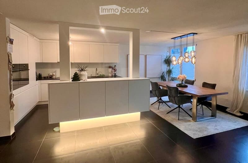 Modern kitchen with kitchen island, dining area with dining table and chairs, white tiled floor, white cabinets, modern lighting, sink with faucet