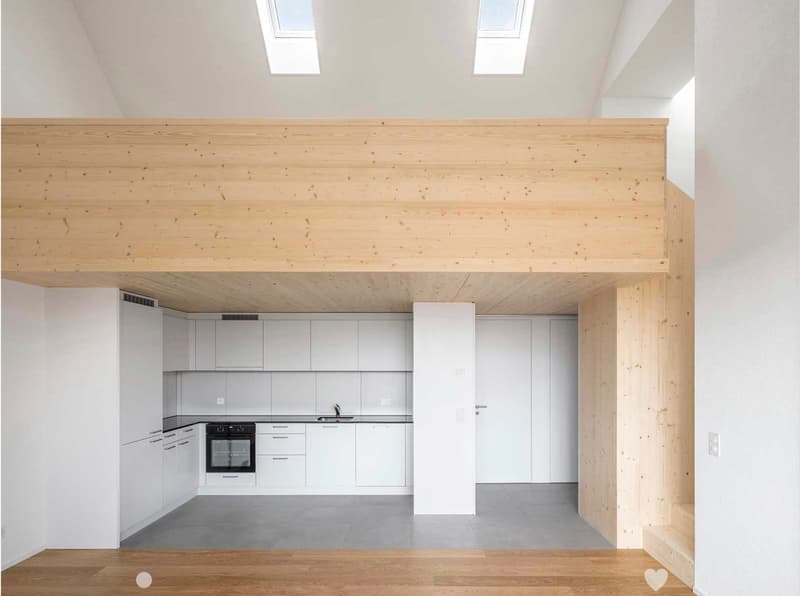 Modern kitchen with white cabinets, stainless steel oven, and sink, featuring a raised wooden platform and skylight windows.