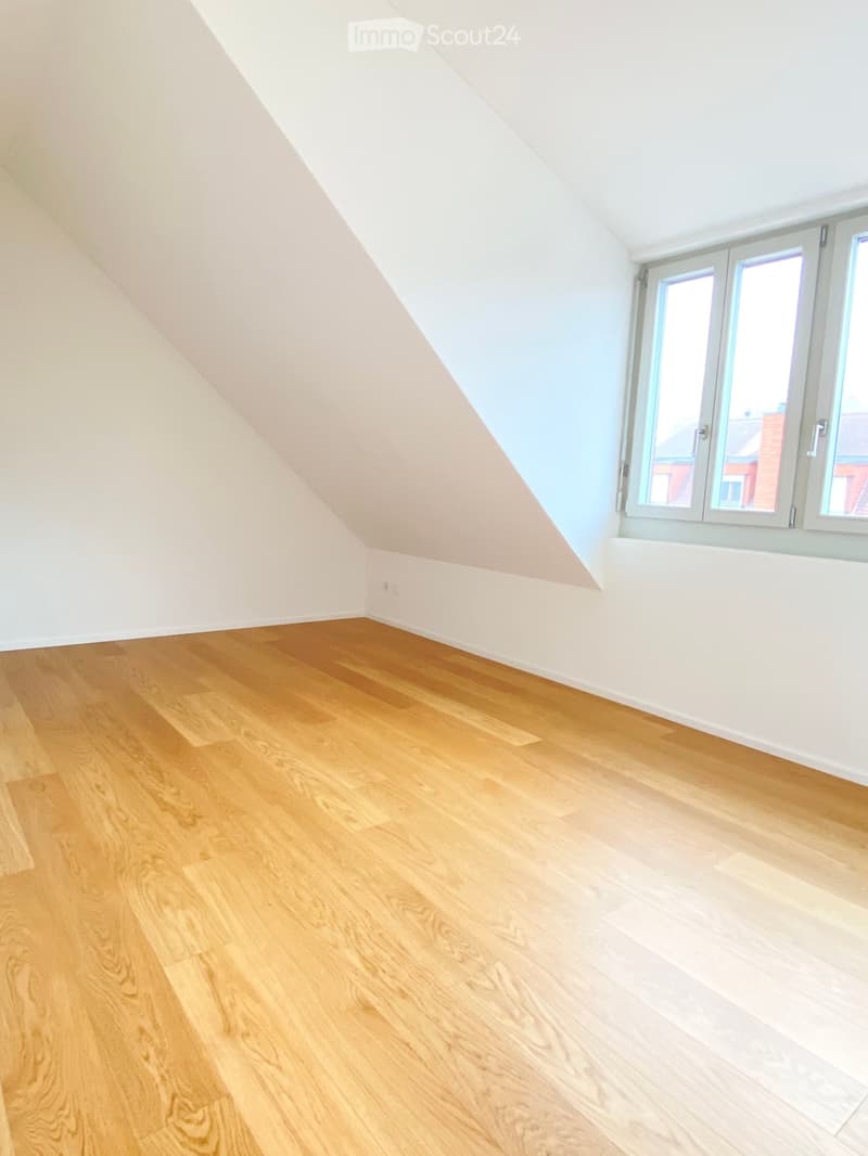 Empty attic room with wooden flooring, white walls, and large windows allowing natural light.