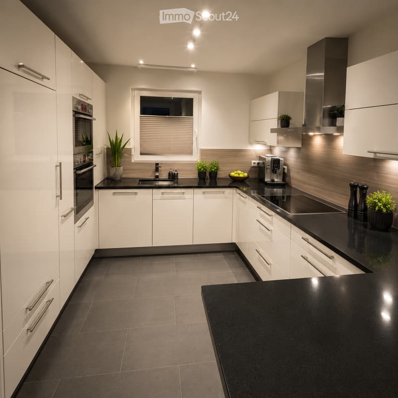 Modern kitchen with white cabinets, black countertops, stainless steel appliances, and built-in lighting. Features include an oven, sink, coffee maker, induction cooktop, and potted plants on the counters.