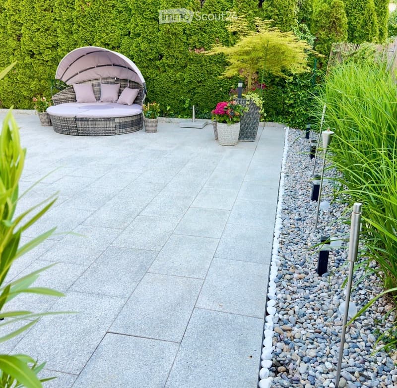 Garden area with a round wicker daybed, cushions, potted plants, and decorative lighting.