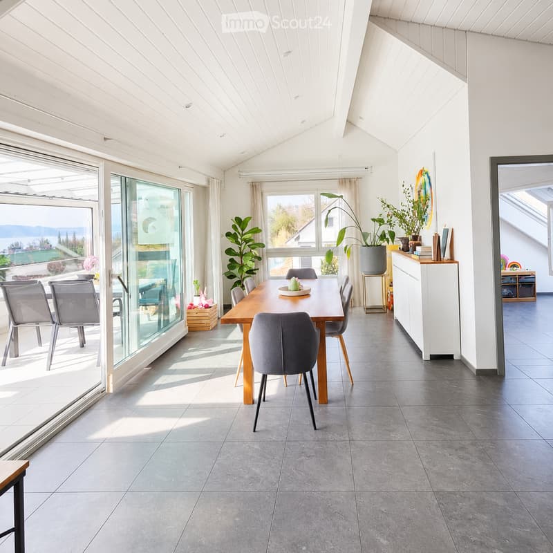 Bright dining area with a wooden table, six chairs, a cabinet, and large windows offering a scenic view.