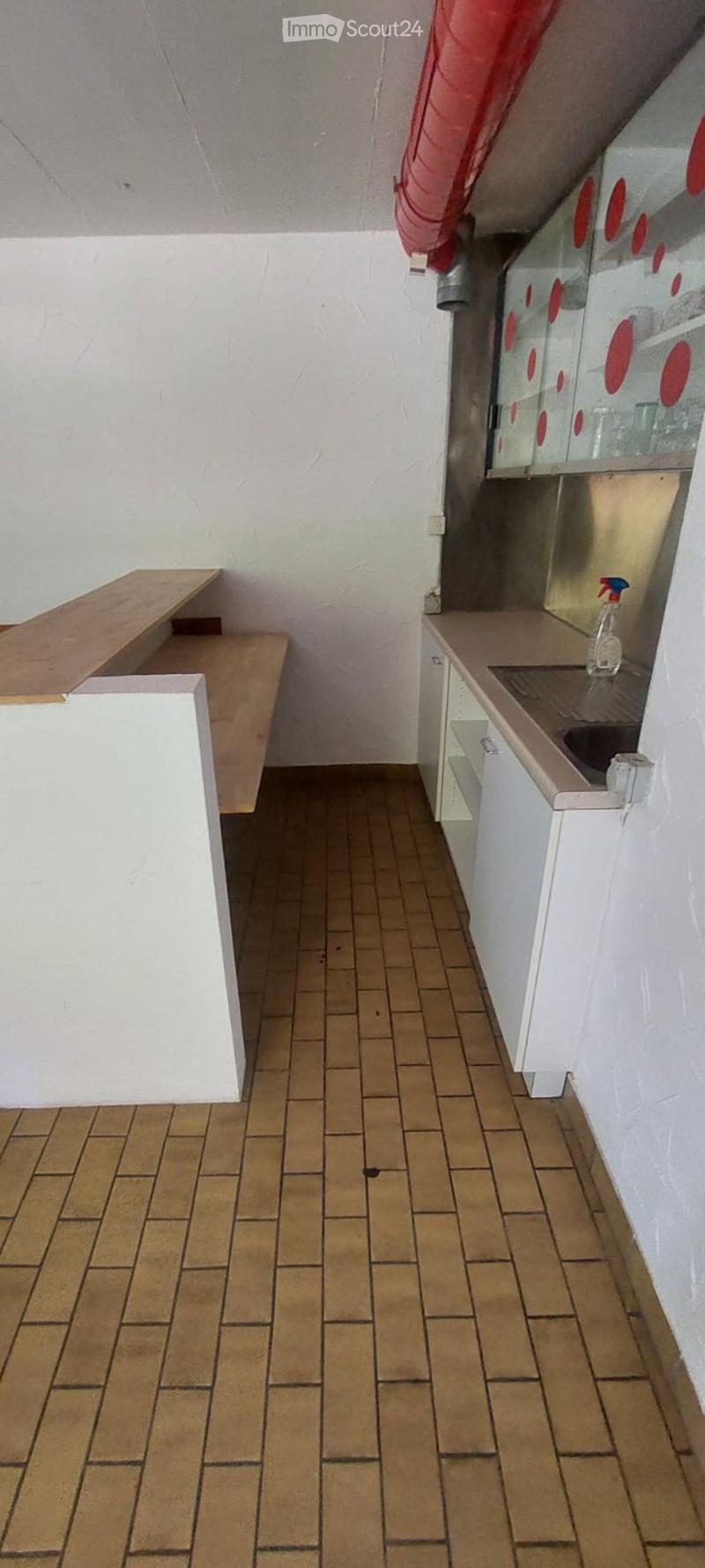 Empty room with tiled floor, white walls, and basic structure including a wooden bench and a small counter area.