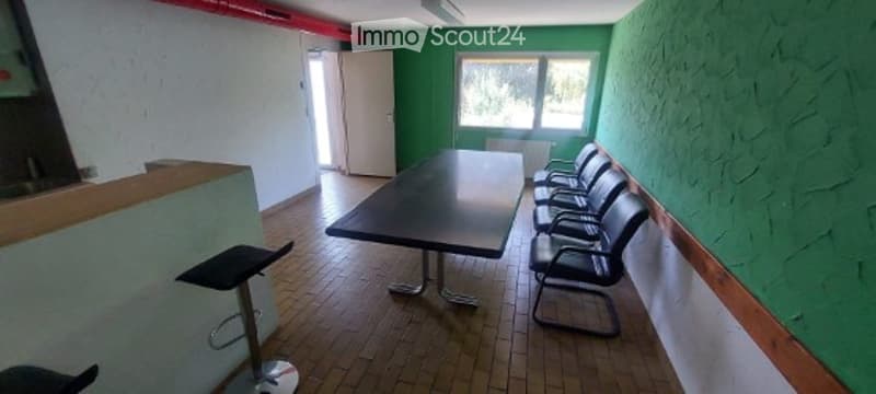 A room with green walls and wooden flooring, featuring a long black table surrounded by black chairs and a black stool near the counter.