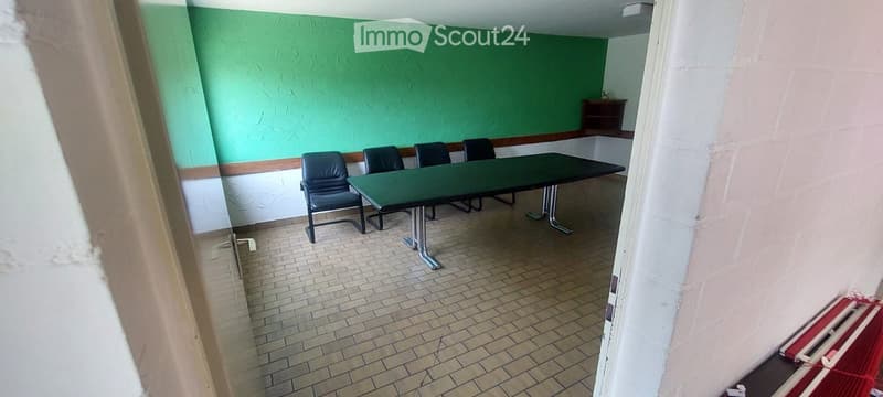 A small meeting or break room with a green table and four black chairs, green walls, and tiled flooring.