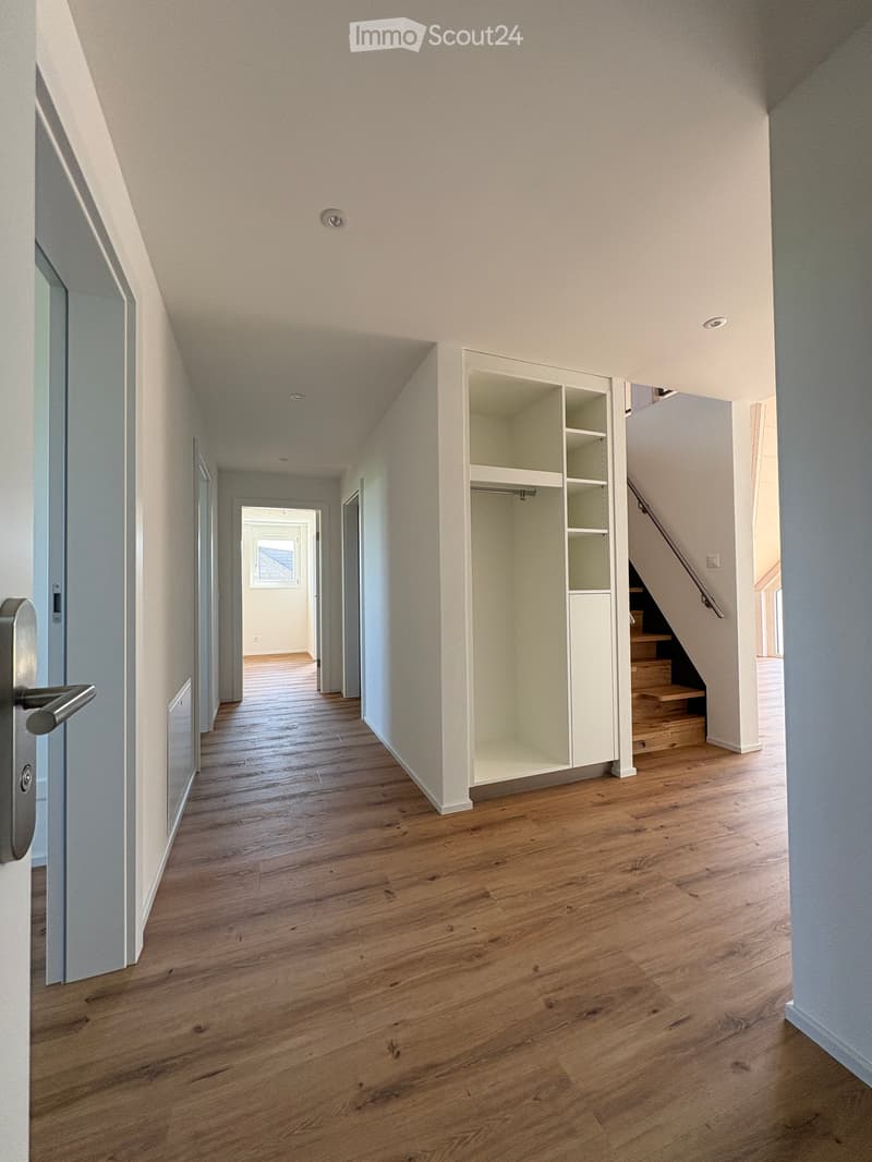 Modern hallway with wooden flooring, white walls, built-in closet, and staircase leading upwards.